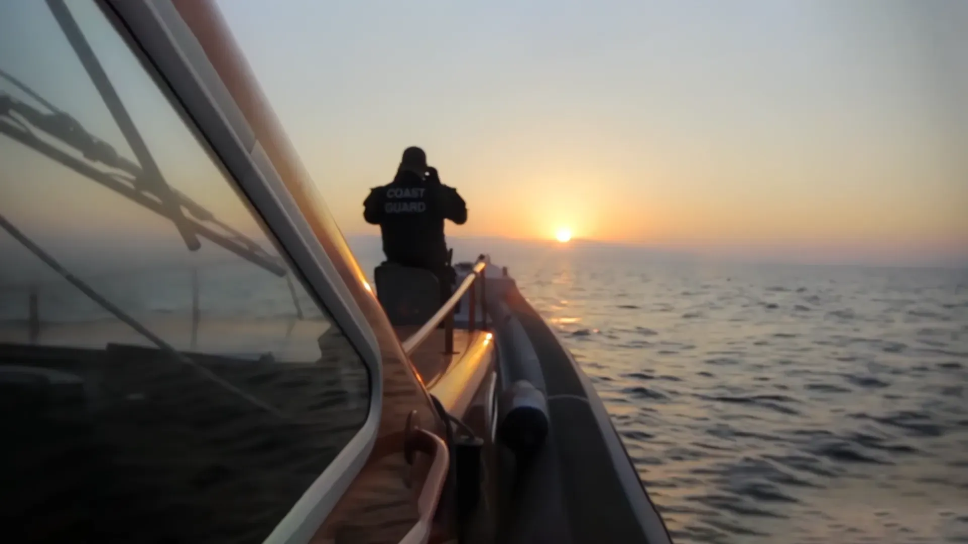 A Coast Guard officer at the bow of a patrol boat at sunrise